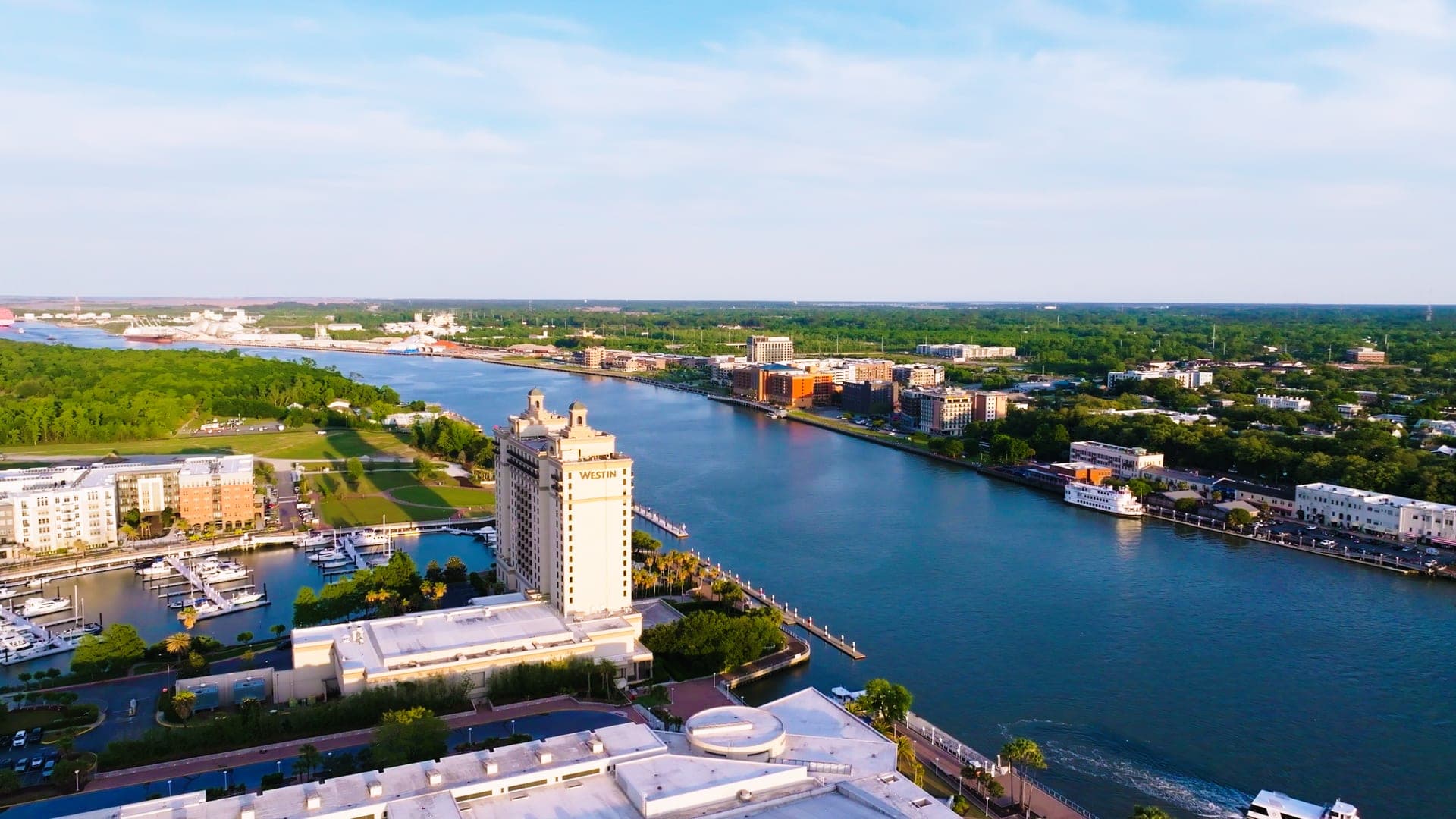 Aerial view of the Savannah River at golden hour, the Westin Savannah Harbor tower on the near bank and the historic riverfront opposite.